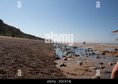 Langer Sandstreifen am Ufer von Cromer, Nortfolk in England, wunderschöne Meereslandschaft mit Felsen, die sich an sonnigen Tagen auf dem Wasser der Strandteiche spiegeln Stockfoto