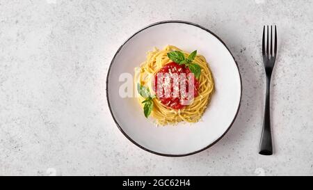 Spaghetti in Tomatensauce, Parmesankäse und Basilikum auf weißem Teller mit schwarzer Gabel auf hellem Hintergrund. Flach liegend, Kopierplatz Stockfoto