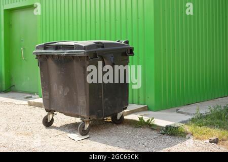 Müllcontainer auf der Straße. Ein Behälter für die Abfallsammlung. Schwarzer Tank auf Rädern. Ort der Abfallentsorgung. Stockfoto