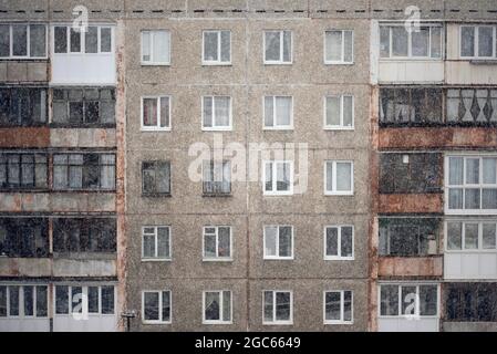 Fassade eines grauen mehrstöckigen sowjetischen Paneelgebäudes im gefallenen Schnee. Russische alte urbane Wohnhäuser mit Fenstern. Typische russische Nachbarschaft Stockfoto