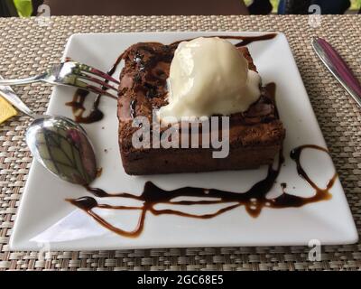 Eine Portion Brownie-Schokoladenkuchen mit Kokoseis auf weißem Servierteller. Stockfoto
