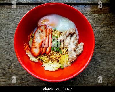 Eiernudeln mit Schweinefleisch trocknen, Schweinefleisch hacken und Ei in roter Schüssel auf dem Holztisch kochen. Stockfoto