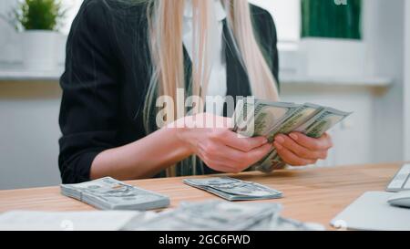 Schnittansicht der Frau in elegantem Anzug am Holztisch sitzend und mit großem Bündel von Dollarscheinen in den Händen Stockfoto