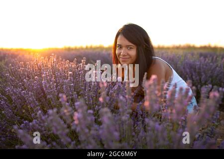 Junge Latina-Frau schaut bei Sonnenuntergang zwischen Lavendelblüten auf die Kamera Stockfoto
