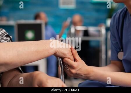 Assistenzmitarbeiter, der während der Therapie behinderte weibliche Senior-Patienten mit den Händen tröstet. Der Rentner ist dankbar für den häuslichen Hilfsdienst. Sozialkrankenpflege zu Hause Stockfoto