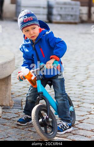 Junge Kind Kind hält sein Fahrrad und sieht wütend aus, trägt blauen Mantel und Mütze Stockfoto