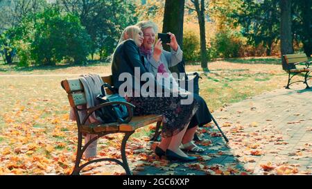 Zoom-Schuss von jungen Frauen und ihrer Großmutter, die etwas auf dem Smartphone im Park sehen. Es gibt einen schönen sonnigen Herbsttag. Stockfoto