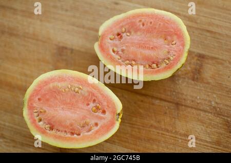 Frische Bio reife rote Guavas Früchte in der Mitte auf einem Holzbrett geschnitten. Exotische Früchte, gesunde Ernährung Konzept Stockfoto