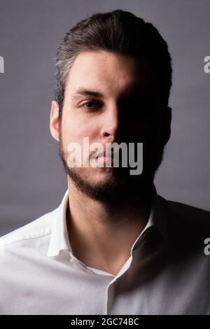 Studioporträt eines kaukasischen Mannes, der ein Hemd mit sicherem und sicherem Ausdruck trägt, die Hälfte des Gesichts im Schatten, Person isoliert auf weißem Hintergrund Stockfoto