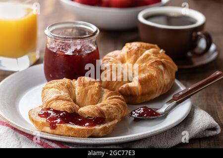 Croissants und Erdbeermarmelade auf einem Teller mit Orangensaft und Kaffee im Hintergrund Stockfoto