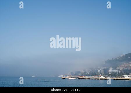 Weiße Schiffe stehen auf dem Dock nahe der Küste im Nebel Stockfoto