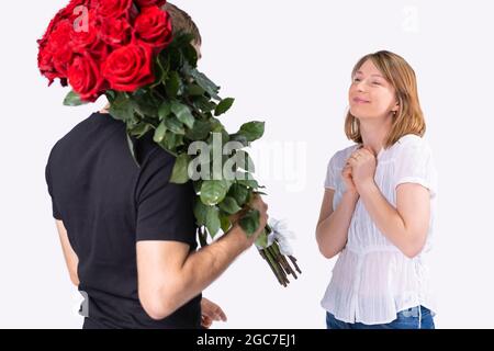 Lieferung Mann in schwarzem T-Shirt mit einem riesigen Strauß Rosen auf der Schulter für die ziemlich erstaunliche junge Frau lächeln und zufrieden für die Stockfoto