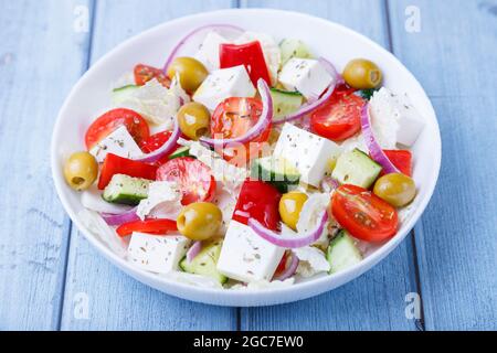 Griechischer Salat. Traditionelles griechisches Gericht. Gesundes vegetarisches Essen. Frisches Gemüse und Feta-Käse auf einem weißen Teller. Nahaufnahme, blauer Hintergrund. Stockfoto