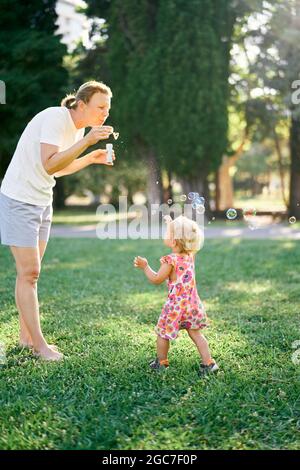 Frau bläst Seifenblasen und kleines Mädchen fangen sie Stockfoto
