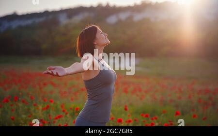 Junge schöne Frau mit erhobenen Armen im Frühjahr Mohnfeld. Sanfte Farben. Nachdenkliche, entspannte Atmosphäre. Stockfoto
