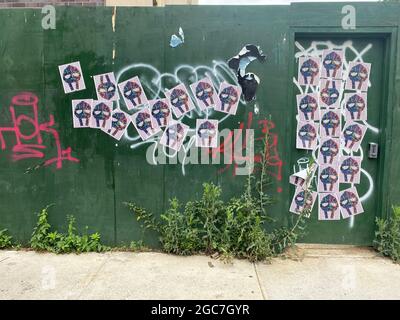 Graffiti und Plakate auf einer Bauwand an einem Bürgersteig in Brooklyn, New York. Stockfoto