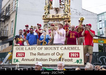 Menschen aller Ethnien drängen die North 8th Street beim jährlichen italienischen Giglio Feast und dem 4 Tonnen schweren Tower Lift in Williamsburg, Brooklyn, NYC. Blaskapelle spielt auf dem 4 Tonnen schweren Giglio-Turm, der auf der Straße angehoben wird. Stockfoto