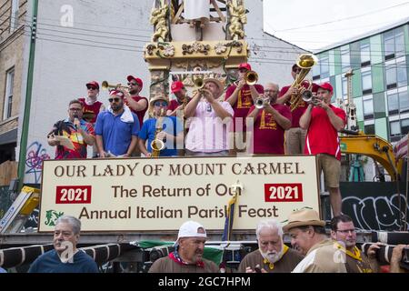 Menschen aller Ethnien drängen die North 8th Street beim jährlichen italienischen Giglio Feast und dem 4 Tonnen schweren Tower Lift in Williamsburg, Brooklyn, NYC. Blaskapelle spielt auf dem 4 Tonnen schweren Giglio-Turm, der auf der Straße angehoben wird. Stockfoto