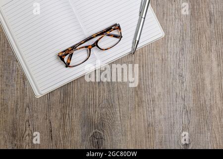 Stift und Brille auf einem Notizbuch auf einer Holzoberfläche. Flach liegend. Stockfoto