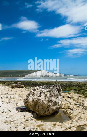 Ein großer Kalksteinfelsen am Strand von Cuckmere Haven, East Sussex, Großbritannien, mit Blick auf Birling Gap und die Seven Sisters bei Ebbe an einem sonnigen Sommer. Stockfoto