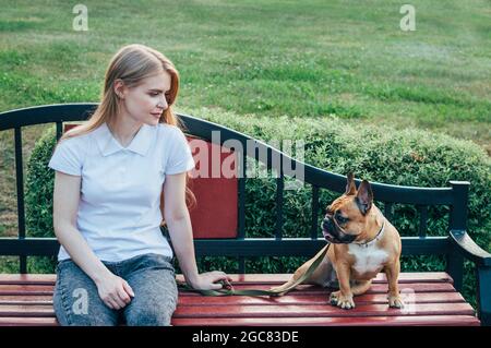 Junge Frau, die im Sommer mit ihrem Hund auf einer Bank im Park ruht Stockfoto