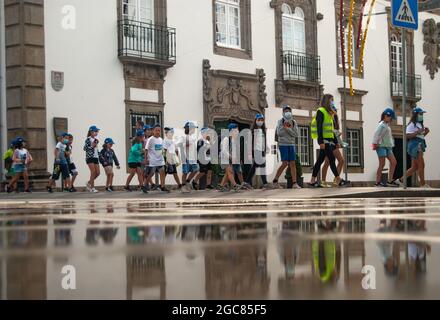 VIANA DO CASTELO, PORTUGAL - 30. JULI 2021: Organisierte Gruppe von Kindern, die mit Senioren in grünen Westen, die sich im Wasser spiegeln, die Straße entlang gehen. Stockfoto