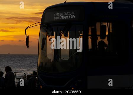 Silhouette eines Stadtbusses, der vor dem gelben Sonnenuntergang vorbeifährt. Bairro do Rio Vermelho, Salvador, Bahia, Brasilien. Stockfoto