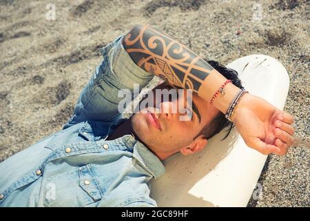 Schöner Mann, der am Strand auf dem Surfbrett liegt Stockfoto