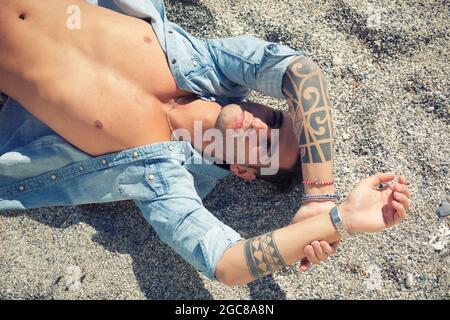 Schöner Mann, der am Strand auf dem Surfbrett liegt Stockfoto