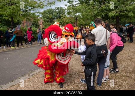 Glasgow, Schottland, Großbritannien. August 2021. Ein Junge legt seine Hand während eines chinesischen Löwentanzes, der bei der Karnevalsparade in Govanhill aufgeführt wird, in den Mund eines Löwen. Die diesjährige Parade umfasst Gemeinschaftsgruppen, einen Pfeifer, Trommler, Tänzer, Jongleure, Rollerskater und eine Blaskapelle starten alle am Govanhill Park und fahren durch die Straßen von Govanhill bis zur Queen's Park Arena. Kredit: Skully/Alamy Live Nachrichten Stockfoto