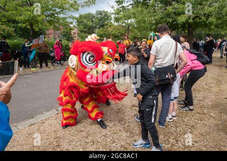 Glasgow, Schottland, Großbritannien. August 2021. Ein Junge legt seine Hand während eines chinesischen Löwentanzes, der bei der Karnevalsparade in Govanhill aufgeführt wird, in den Mund eines Löwen. Die diesjährige Parade umfasst Gemeinschaftsgruppen, einen Pfeifer, Trommler, Tänzer, Jongleure, Rollerskater und eine Blaskapelle starten alle am Govanhill Park und fahren durch die Straßen von Govanhill bis zur Queen's Park Arena. Kredit: Skully/Alamy Live Nachrichten Stockfoto