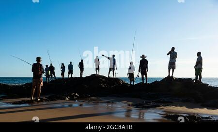 Salvador, Bahia, Brasilien - 25. April 2021: Fischer auf Felsen mit ihren Angelruten versuchen, Fische zu fangen, um sie zu verkaufen und zu konsumieren. Stockfoto