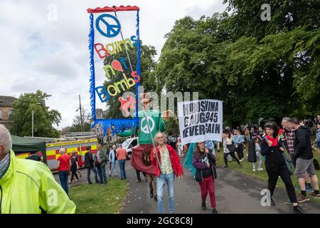 Glasgow, Schottland, Großbritannien. August 2021. Ein Schild mit der Aufschrift Bairns keine Bomben und ein anderes Schild mit der Aufschrift Hiroshima 6 Aug 1945 nie wieder werden in der Govanhill Carnival Parade getragen. Die diesjährige Parade umfasst Gemeinschaftsgruppen, einen Pfeifer, Trommler, Tänzer, Jongleure, Rollerskater und eine Blaskapelle starten alle am Govanhill Park und fahren durch die Straßen von Govanhill bis zur Queen's Park Arena. Kredit: Skully/Alamy Live Nachrichten Stockfoto