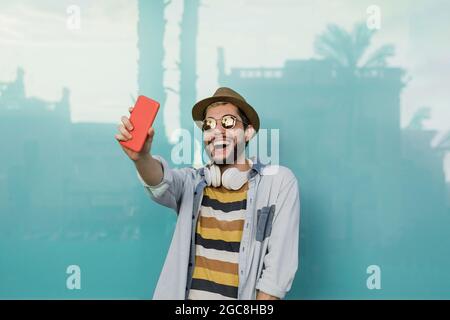 Junger Hipster-Mann macht ein Selfie mit Handy im Freien mit blauem Hintergrund - Fokus auf Gesicht Stockfoto