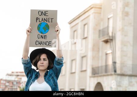 Junge Demonstrator-Aktivistin mit Transparent während des Protestes zum Klimawandel im Freien in der Stadt - Fokus auf Hipster-Mädchengesicht Stockfoto