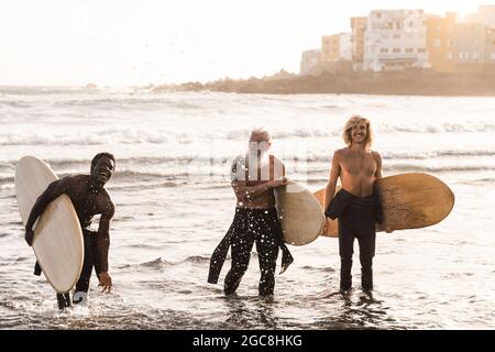 Multirassische Surfer-Freunde halten Surfbretter nach extremer Wassersport-Session mit Strand im Hintergrund - Weiche Konzentration auf Hipster Senior Mann Stockfoto