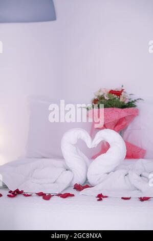 Nahaufnahme der romantischen Komposition auf dem Bett im Hotel. Weiße Handtücher in Schwanenform. Blumenstrauß. Rosenblüten. Stockfoto