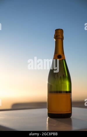 Nahaufnahme einer Flasche Champagner auf dem weißen Tisch auf der Terrasse. Sekt. Sonnenuntergang Himmel auf Hintergrund. Stockfoto