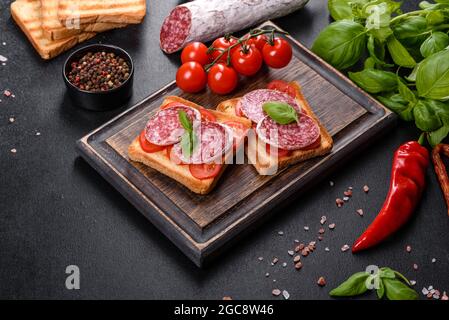 Spanische getrocknete Wurstsalami auf einem dunklen Betongrund. Zubereitung von leckeren frischen Sandwiches Stockfoto