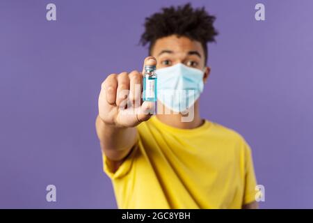 Medizin, Coronavirus und Menschen Konzept. Nahaufnahme des jungen Mannes in der Gesichtsmaske, die Ampulle mit dem Medikament hält, schließlich Impfstoff aus Kovid19 gefunden Stockfoto