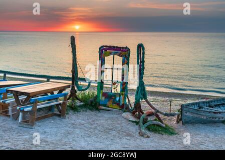 Vama Veche, Rumänien - Blaue Tür mit buntem Glas und Anker am Strand bei Sonnenaufgang, Schwarzmeerküste. Stockfoto