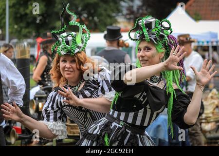 Schiffshebewerk Henrichenburg, Waltrop, Deutschland, 7. August 2021. Zwei Teilnehmer des Stalls ´Lady Frankenstein´ posieren in ihren farbenfrohen Outfits. Steampunk-Fans und Besucher, viele in voll retro-futuristischen Kostümen und Outfits, treffen sich zum´Steampunk Jubilee Market´ Festival am historischen Wahrzeichen der Henrichenburg-Seilbahn, Teil des Waltrop-Schlossparks am Dortmund-Ems-Kanal, heute ein Industriemuseum. Das alte Eisengerüst, die Kontrolltürme, Maschinenhäuser und das Museum bilden eine stimmungsvolle Kulisse für das Festival, Stockfoto