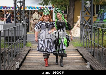 Schiffshebewerk Henrichenburg, Waltrop, Deutschland, 7. August 2021. Zwei Teilnehmer des Stalls ´Lady Frankenstein´ posieren in ihren farbenfrohen Outfits. Steampunk-Fans und Besucher, viele in voll retro-futuristischen Kostümen und Outfits, treffen sich zum´Steampunk Jubilee Market´ Festival am historischen Wahrzeichen der Henrichenburg-Seilbahn, Teil des Waltrop-Schlossparks am Dortmund-Ems-Kanal, heute ein Industriemuseum. Das alte Eisengerüst, die Kontrolltürme, Maschinenhäuser und das Museum bilden eine stimmungsvolle Kulisse für das Festival, Stockfoto