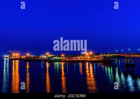 Liegt am Hafen von saint John, NB, Kanada in der Nacht. Helle Lichter an den Docks spiegeln sich im Hafen, dunkelblauer Himmel darüber, Hafenbrücke rechts. Stockfoto