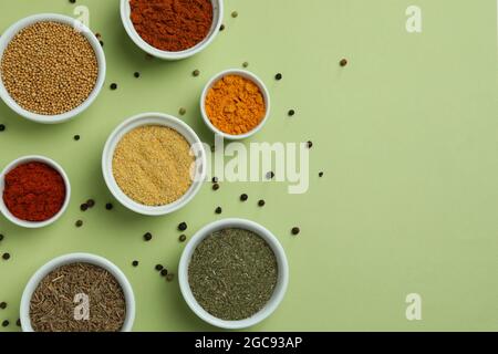 Set aus verschiedenen Gewürzen in Schüsseln auf grünem Hintergrund Stockfoto