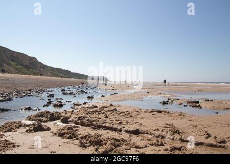 Langer Sandstreifen am Ufer von Cromer, Nortfolk in England, wunderschöne Meereslandschaft mit Felsen, die sich an sonnigen Tagen auf dem Wasser der Strandteiche spiegeln Stockfoto