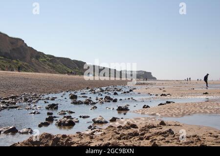 Langer Sandstreifen am Ufer von Cromer, Nortfolk in England, wunderschöne Meereslandschaft mit Felsen, die sich an sonnigen Tagen auf dem Wasser der Strandteiche spiegeln Stockfoto