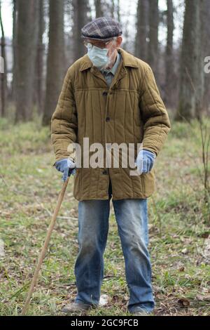 Ein alter Mann in Russland. Ein Mann mit einem Gehstock. Rentner in einer alten Jacke. Russischer alter Mann in einer medizinischen Maske auf der Straße. Ein alter Mensch mit einem di Stockfoto