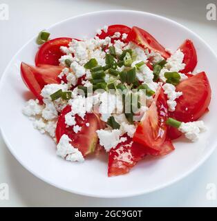 Frischer Tomatensalat mit Quark und Frühlingszwiebeln in einer weißen Schüssel auf weißem Hintergrund. Hausgemachtes Essen. Draufsicht. Leckere und gesunde Mahlzeit. Stockfoto