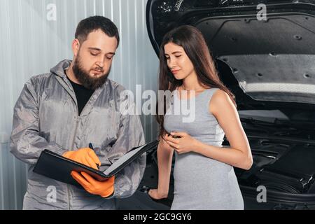 Auto Mechanic erklärt weiblichen Kunden die Fahrzeugreparaturrechnung und unterschreibt Papiere Stockfoto